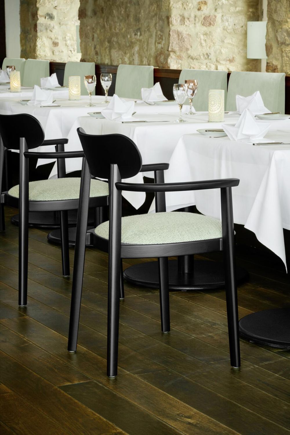 Elegante, schwarze Stühle an einem stilvoll gedeckten Tisch in einem Restaurant mit Holzboden und Steinwand.