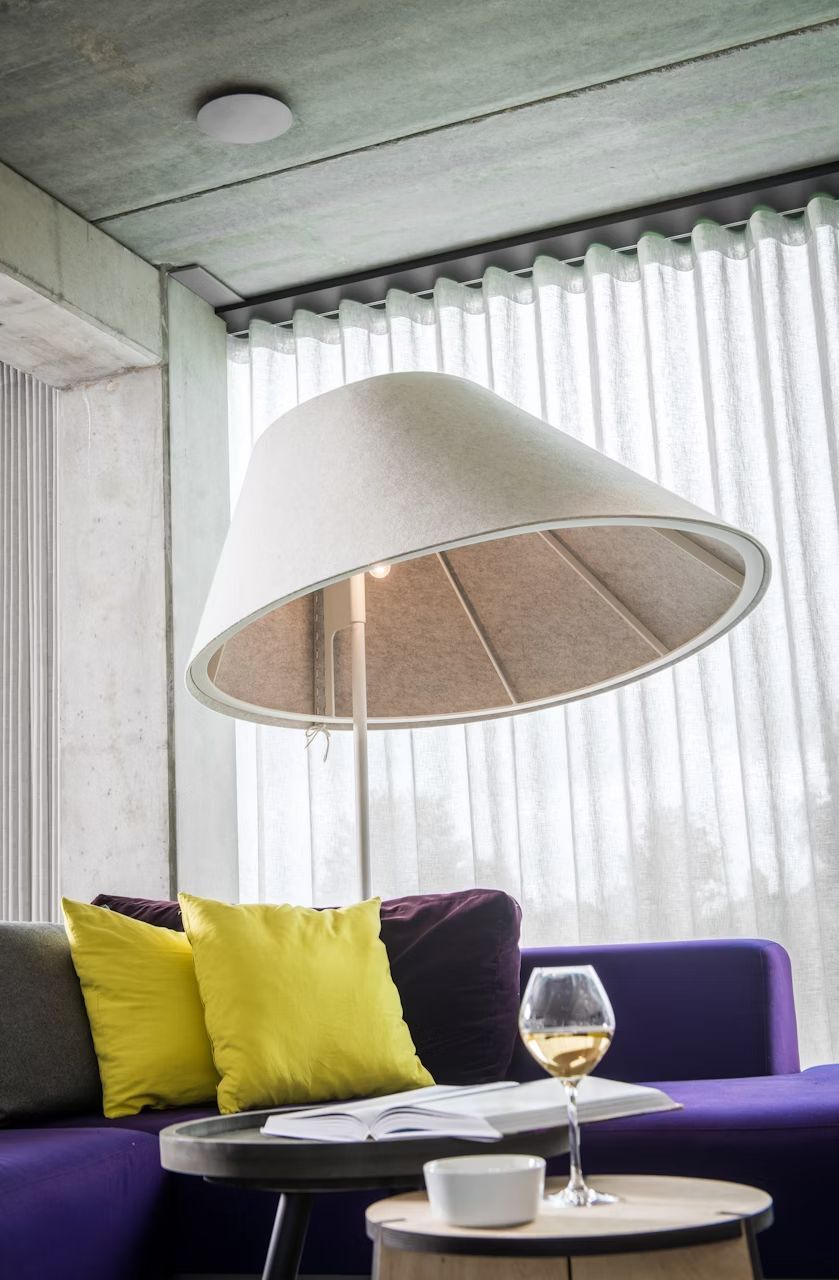 Moderner Wohnraum mit großer Bogenlampe, violettem Sofa, gelben Kissen und Tisch mit Buch und Weinglas.