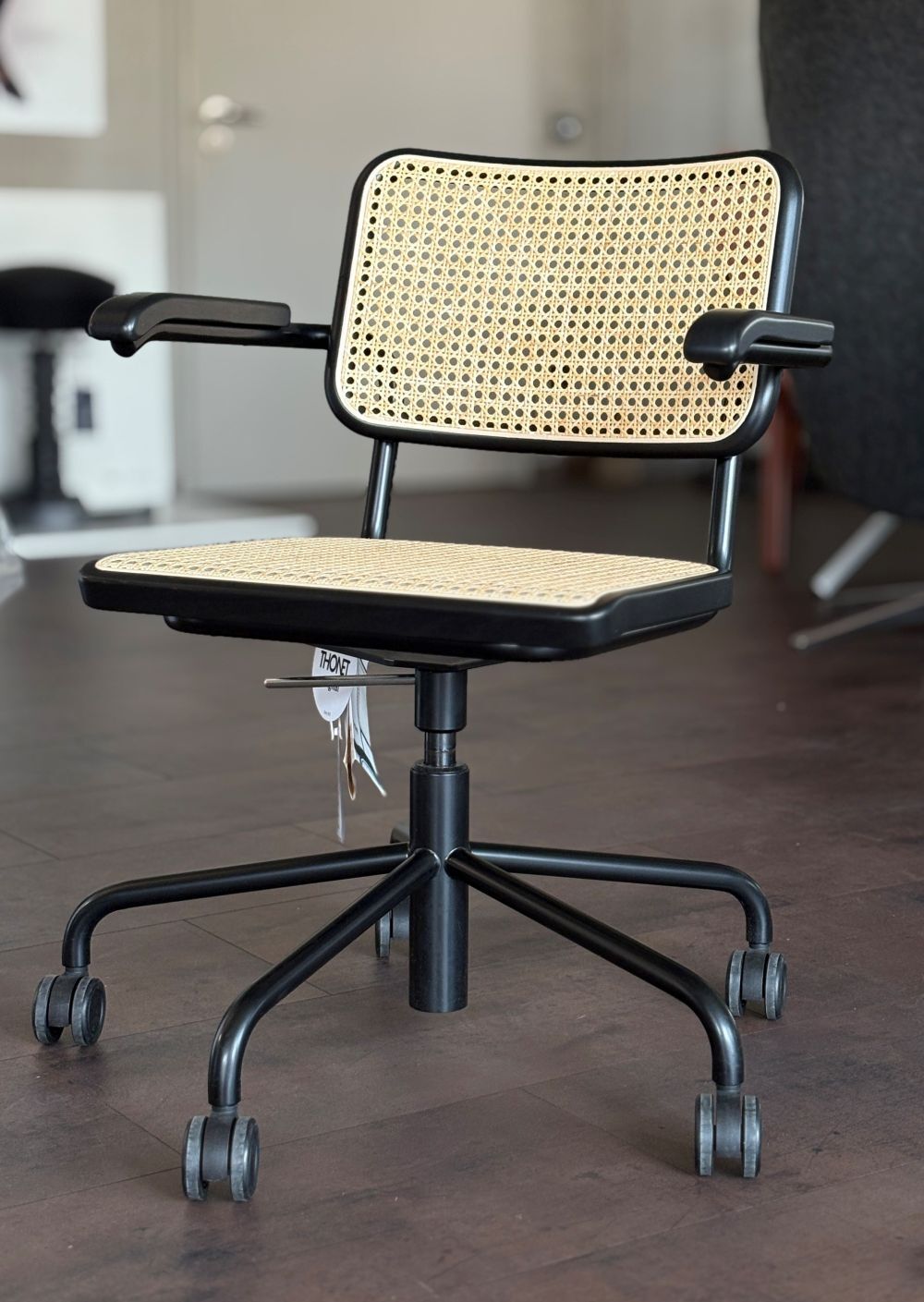 Schwarzer ergonomischer Bürostuhl mit Holzgeflecht-Sitzfläche, Armlehnen und Rollen, geeignet für dynamisches Sitzen.