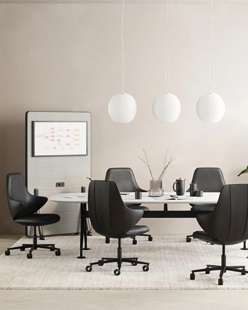 Moderner Konferenzraum mit fünf ergonomischen Bürostühlen um einen Tisch, drei hängende Lampen und Wandstaffelei.