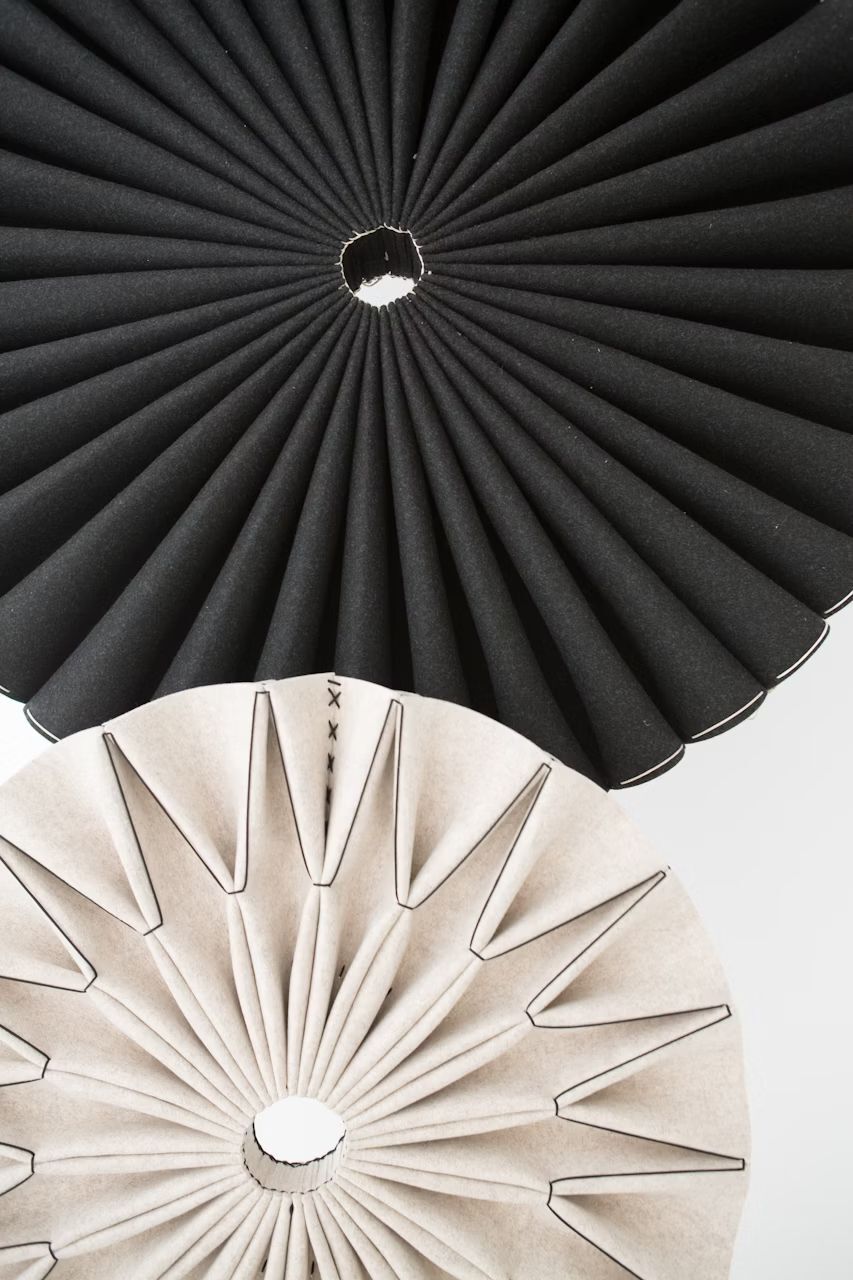 Zwei übereinanderliegende kreisförmige Strukturen, eine schwarz und eine beige, erinnern an gefaltetes Papier.