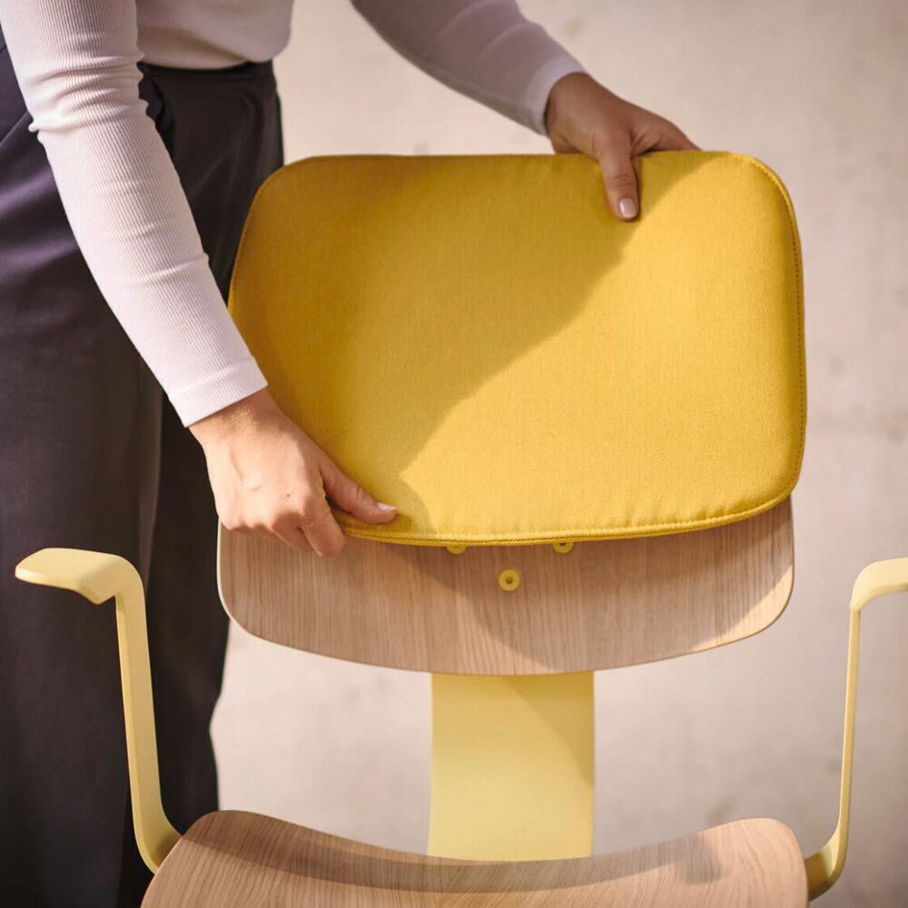 Person justiert gelbes Rückenkissen auf ergonomischem Holzstuhl mit gelben Akzenten für verbesserten Sitzkomfort.