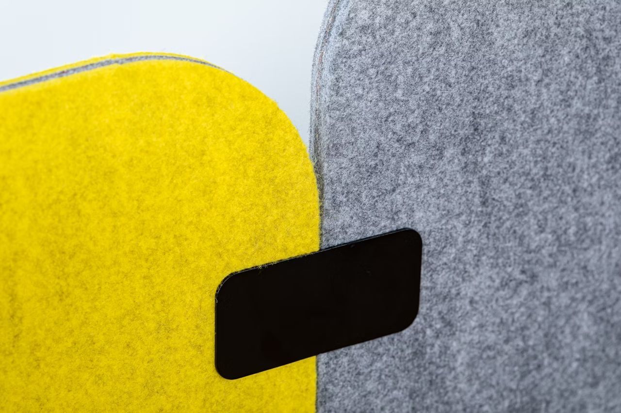 Zwei Filztrennwände, eine gelb und eine grau, mit schwarzem Verbindungselement, bieten modernen Bürokomfort.