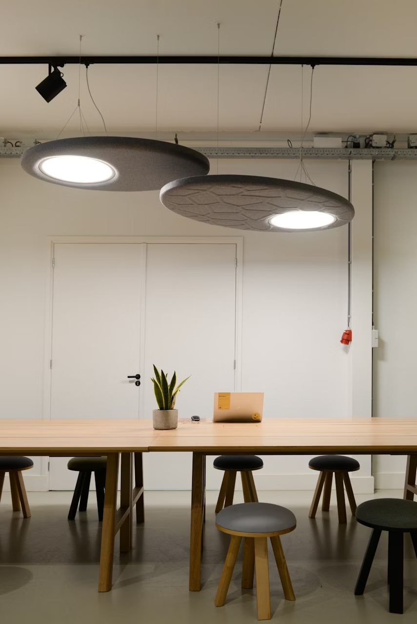 Moderner Konferenzraum mit großen, runden Hängelampen, einem Holztisch und Hockern, dekoriert mit einer Pflanze.