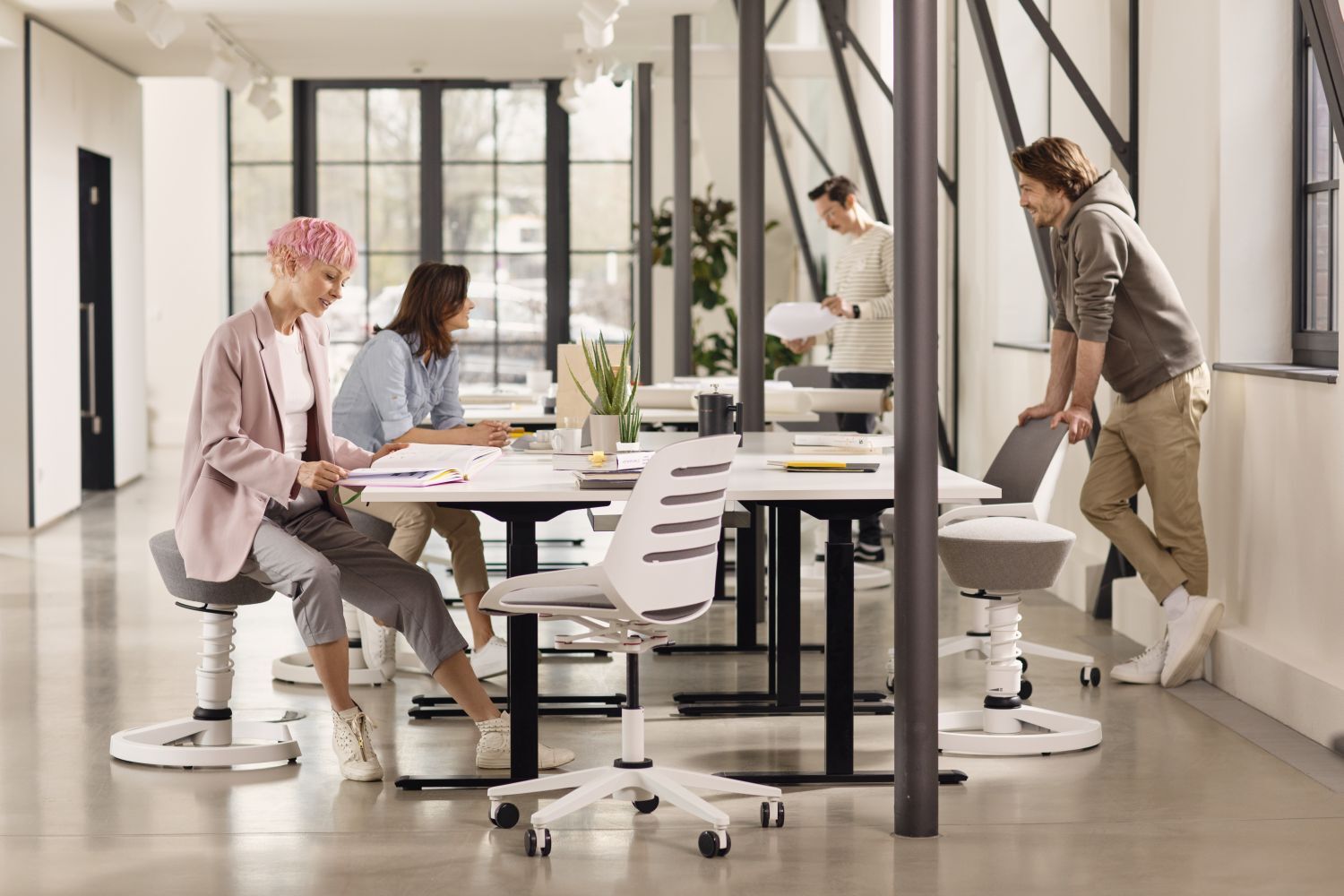 Menschen arbeiten in einem modernen Büro mit ergonomischen Stühlen, die dynamisches Sitzen fördern.