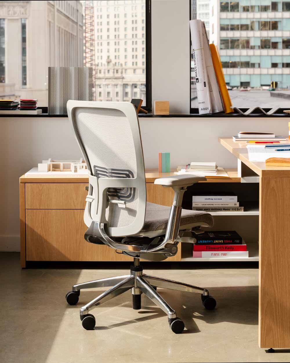 Ergonomischer Bürostuhl vor Schreibtisch in modernem Büro mit großen Fenstern und Stadtblick.