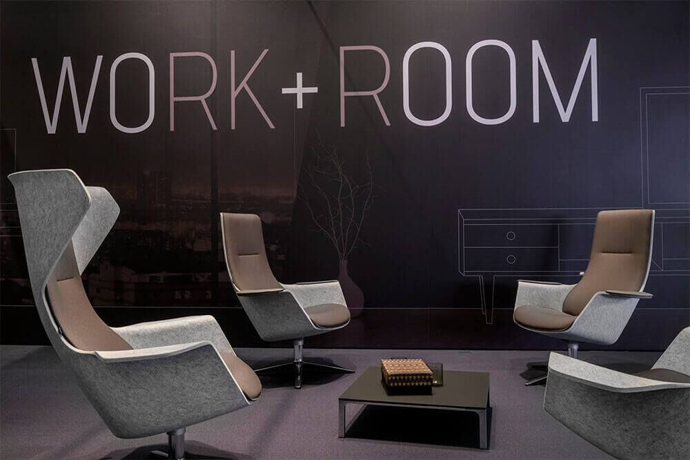 Ergonomische Bürostühle in einem modernen Raum mit „WORK+ROOM“-Schriftzug an der Wand.