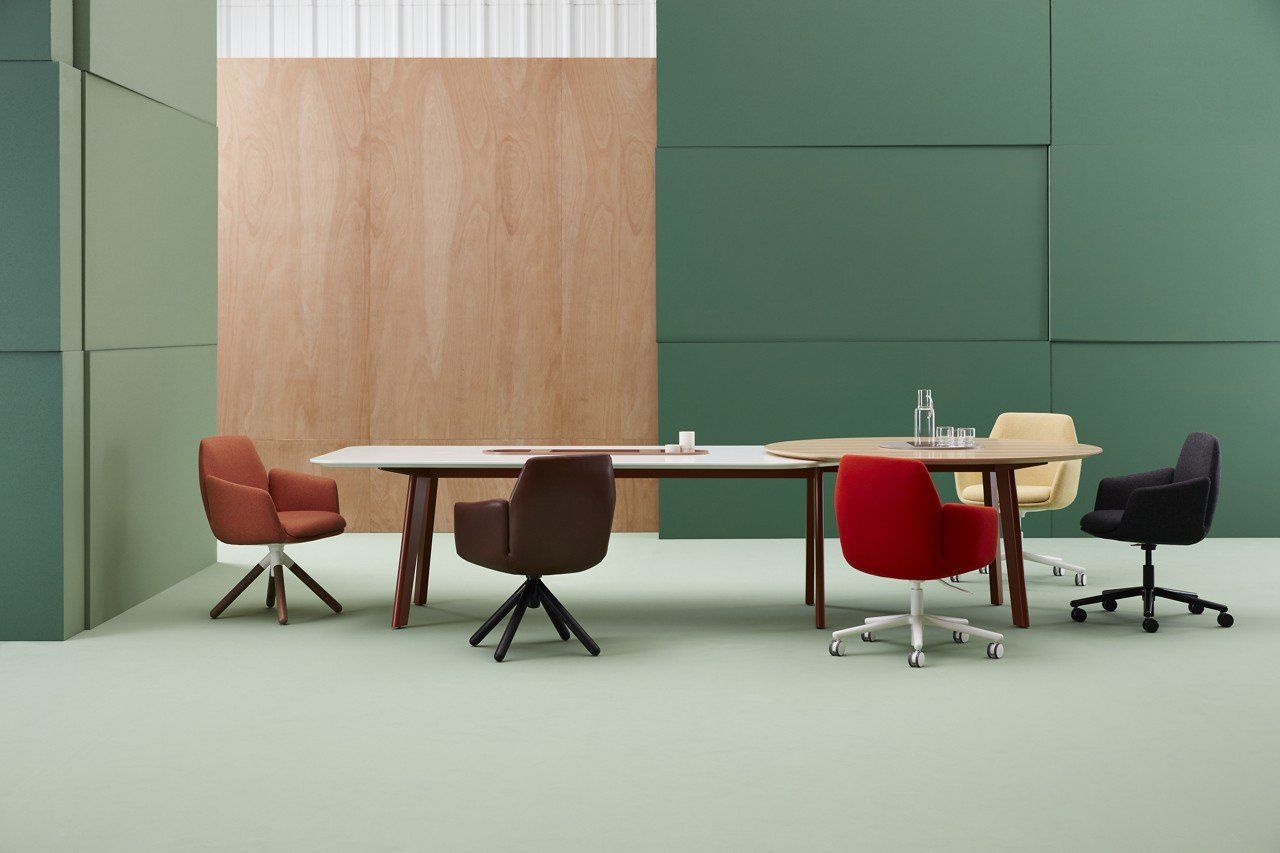 Bürogestaltung mit sechs farbigen ergonomischen Stühlen um zwei Holztische vor grünem und holzgetäfeltem Hintergrund.