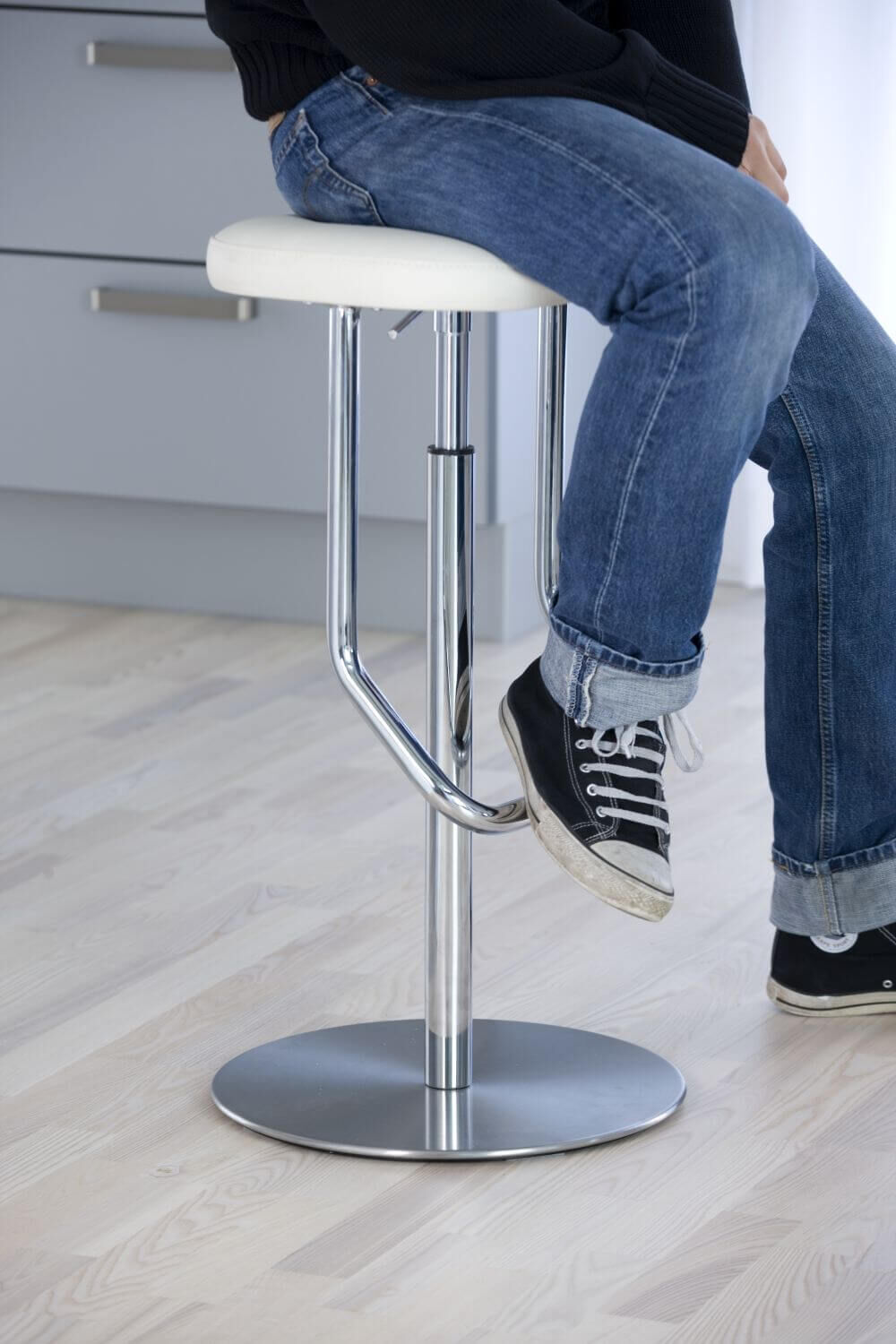 Person sitzt auf ergonomischem Hocker mit Chromfuß und gepolstertem Sitz, fördert dynamisches Sitzen.