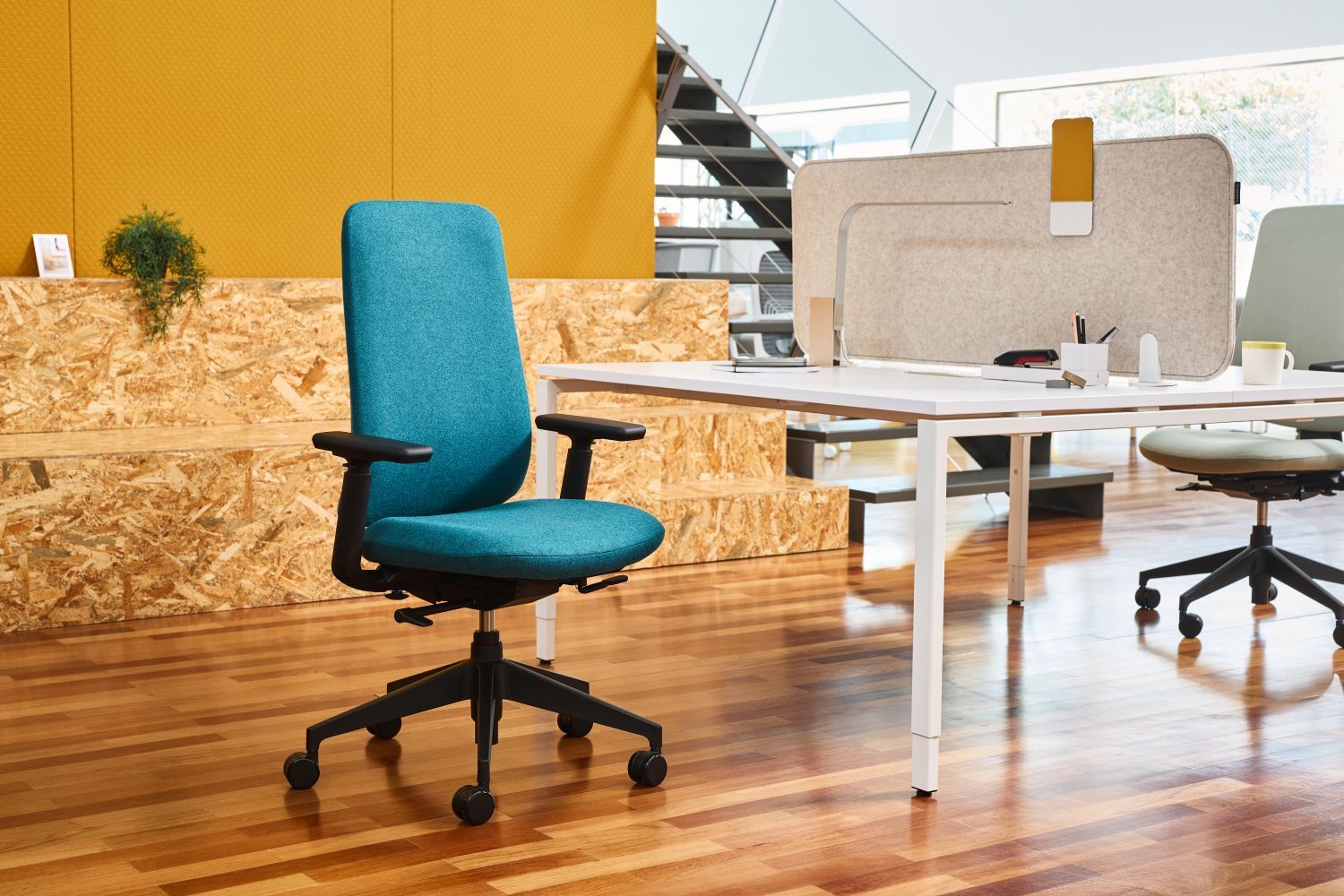 Ergonomischer Bürostuhl in Türkis neben einem modernen Schreibtisch in einem hellen Büro.