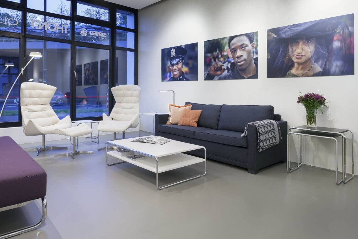 Ein stilvoller Wartebereich mit ergonomischen weißen Stühlen, einem modernen Sofa und großformatigen Wandbildern.