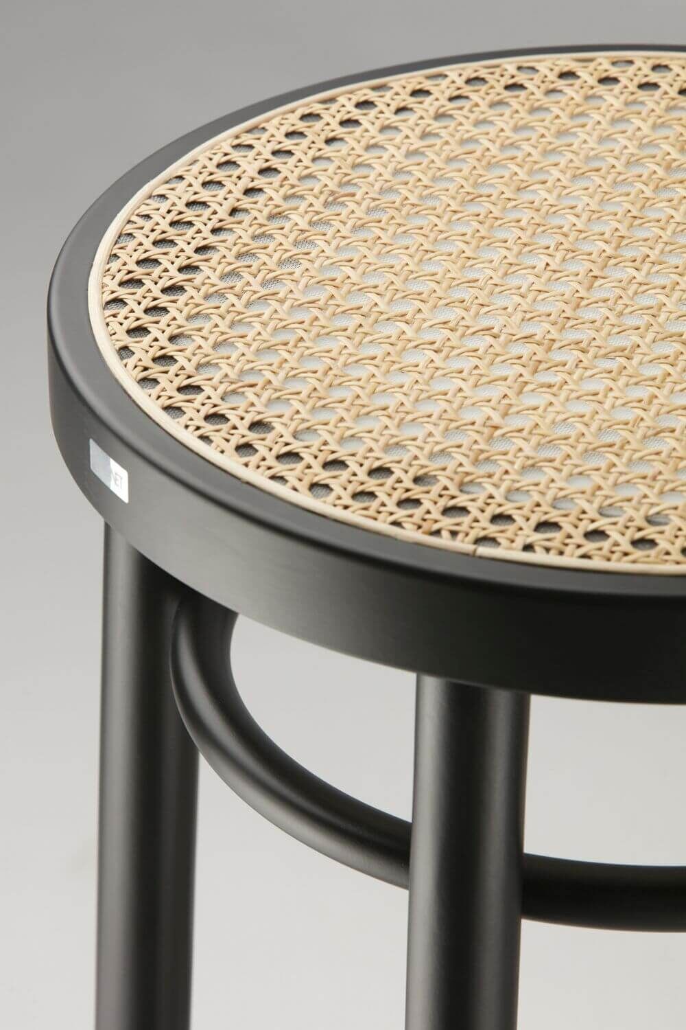 Detailansicht eines Hockers mit schwarzem Rahmen und geflochtener Sitzfläche aus naturfarbenem Rattan.