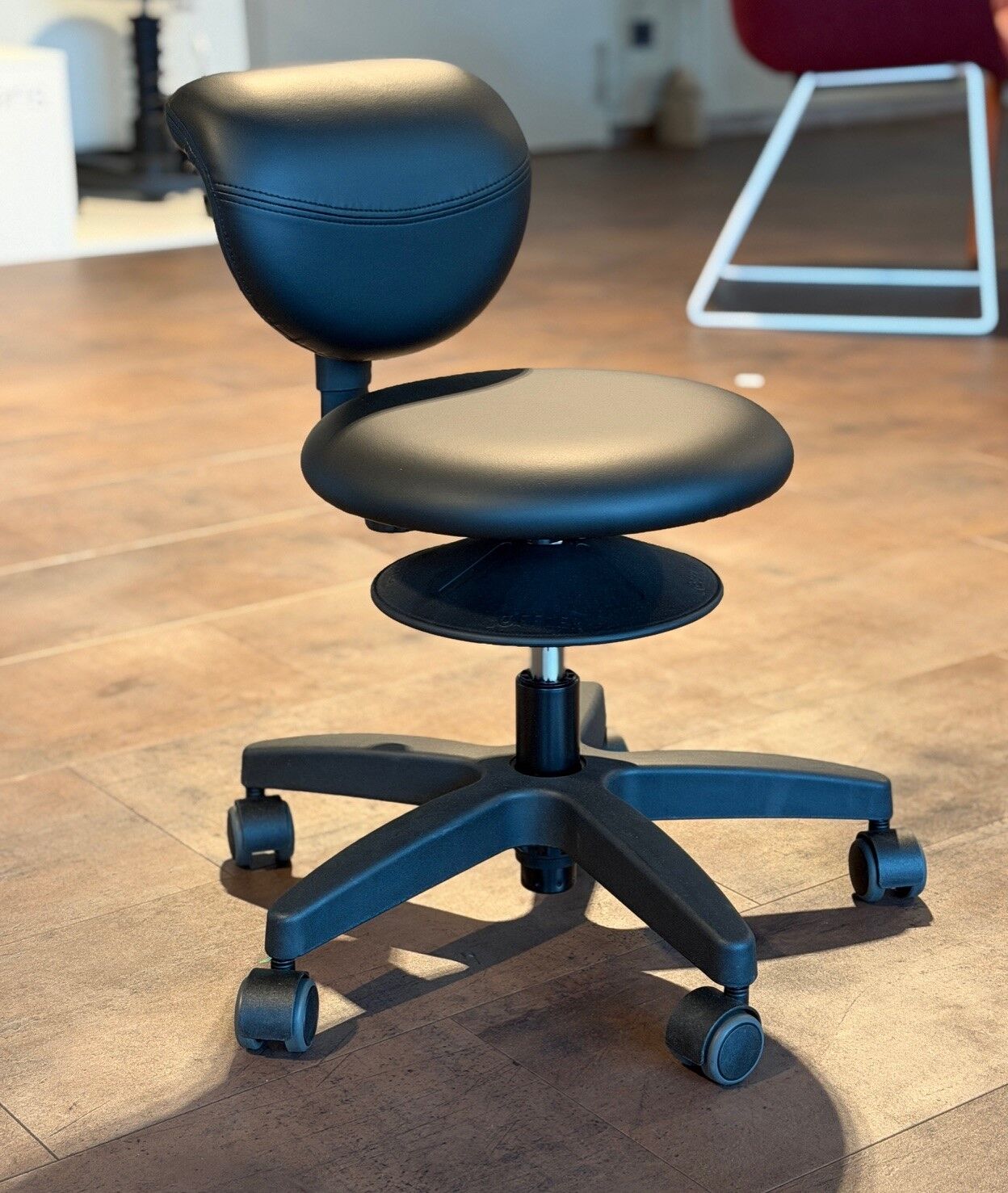 Ergonomischer Bürostuhl mit runder Rückenlehne und Rollen, auf einem Holzboden stehend, für dynamisches Sitzen.