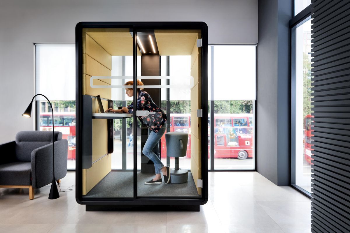 Frau arbeitet stehend im ergonomischen Büro-Pod, umgeben von modernem Design, fördert bewegtes Sitzen und Konzentration.