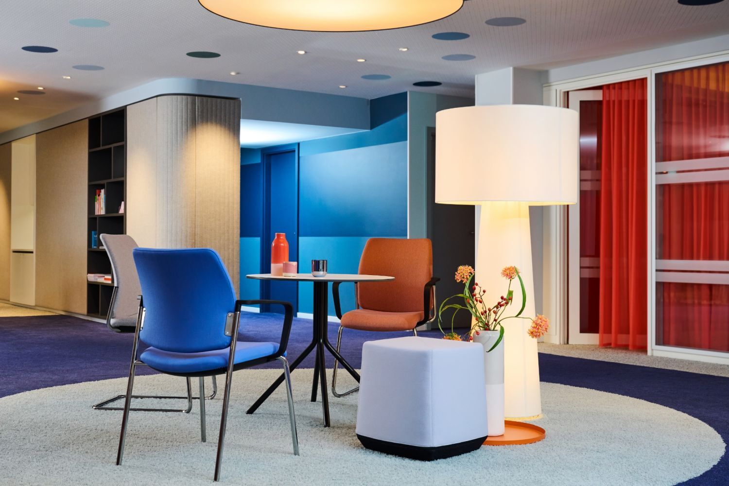 Moderne Büroeinrichtung mit ergonomischen Stühlen, rundem Tisch, Stehleuchte und farbiger Dekoration in einem stilvollen Raum.