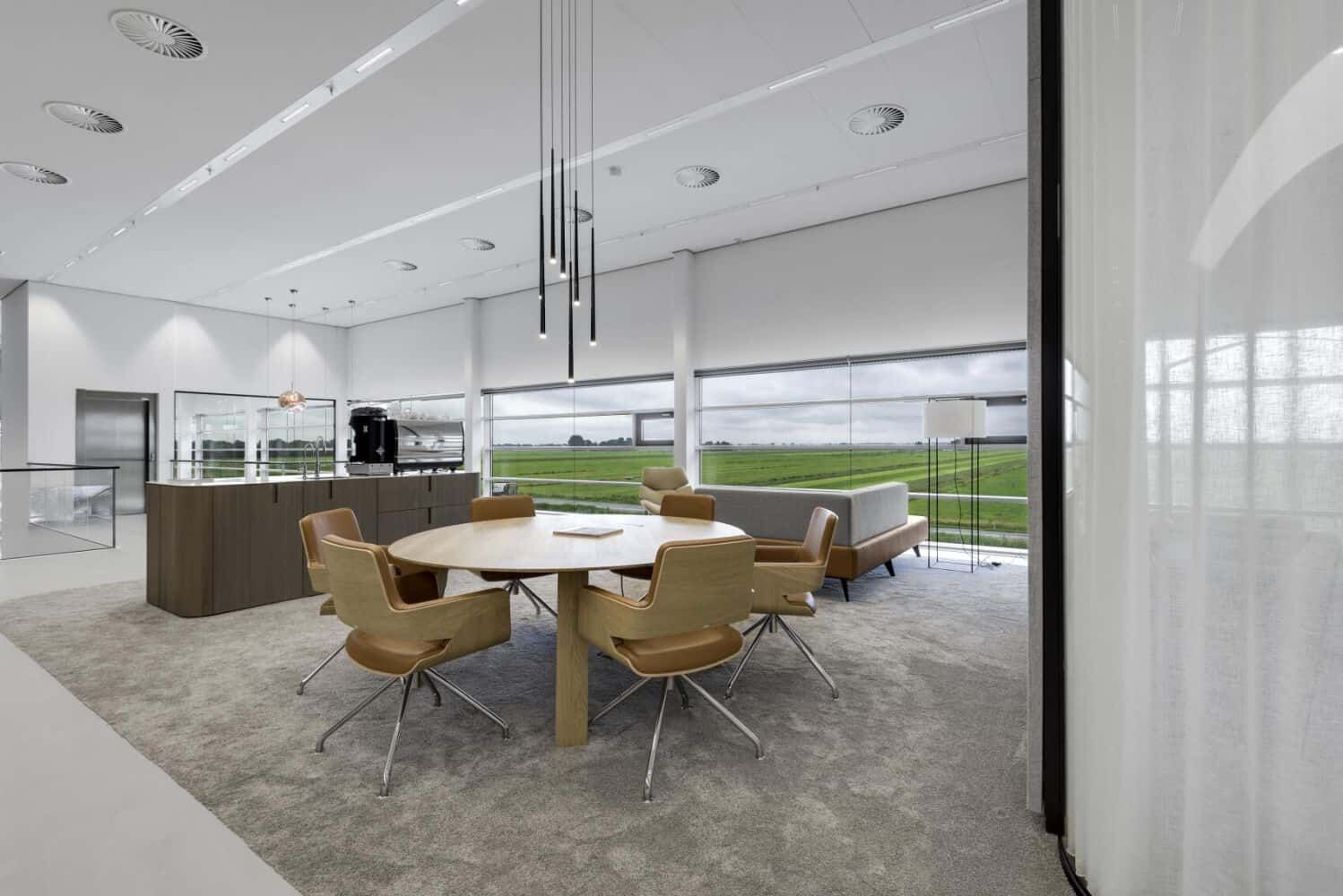 Moderner Büroraum mit ergonomischen Stühlen und großem Tisch, Blick auf grüne Landschaft durch Panoramafenster.