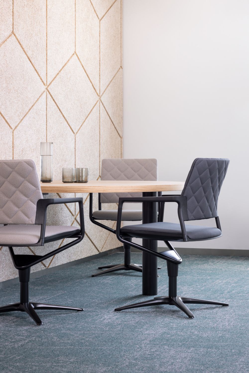 Moderner Besprechungsraum mit ergonomischen Drehstühlen und Holztisch, hervorhebend durch geometrische Wandmuster.