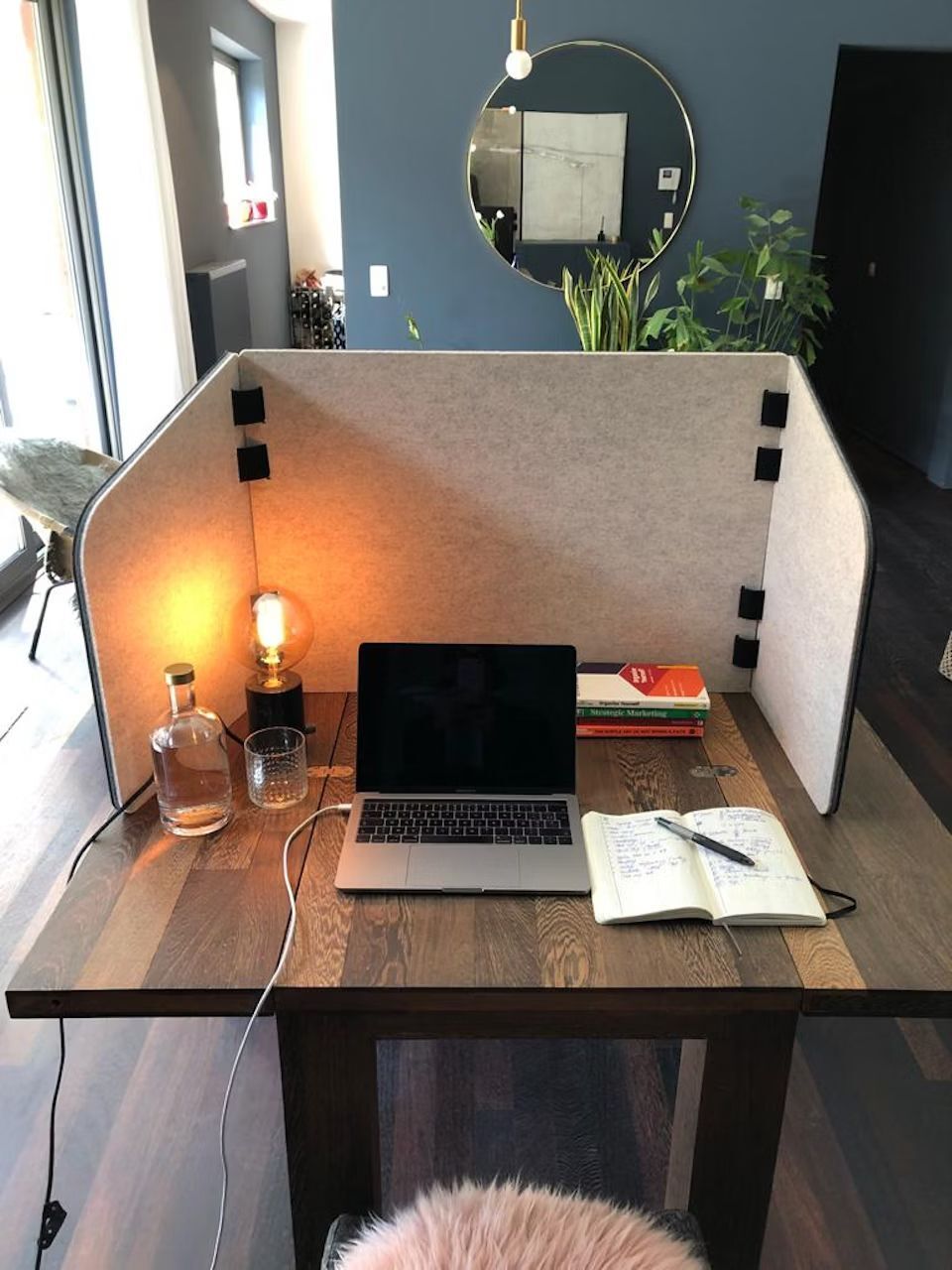 Ergonomischer Arbeitsplatz mit Laptop, Lampe, Notizbuch und Büchern auf einem Holztisch, umgeben von Sichtschutz.
