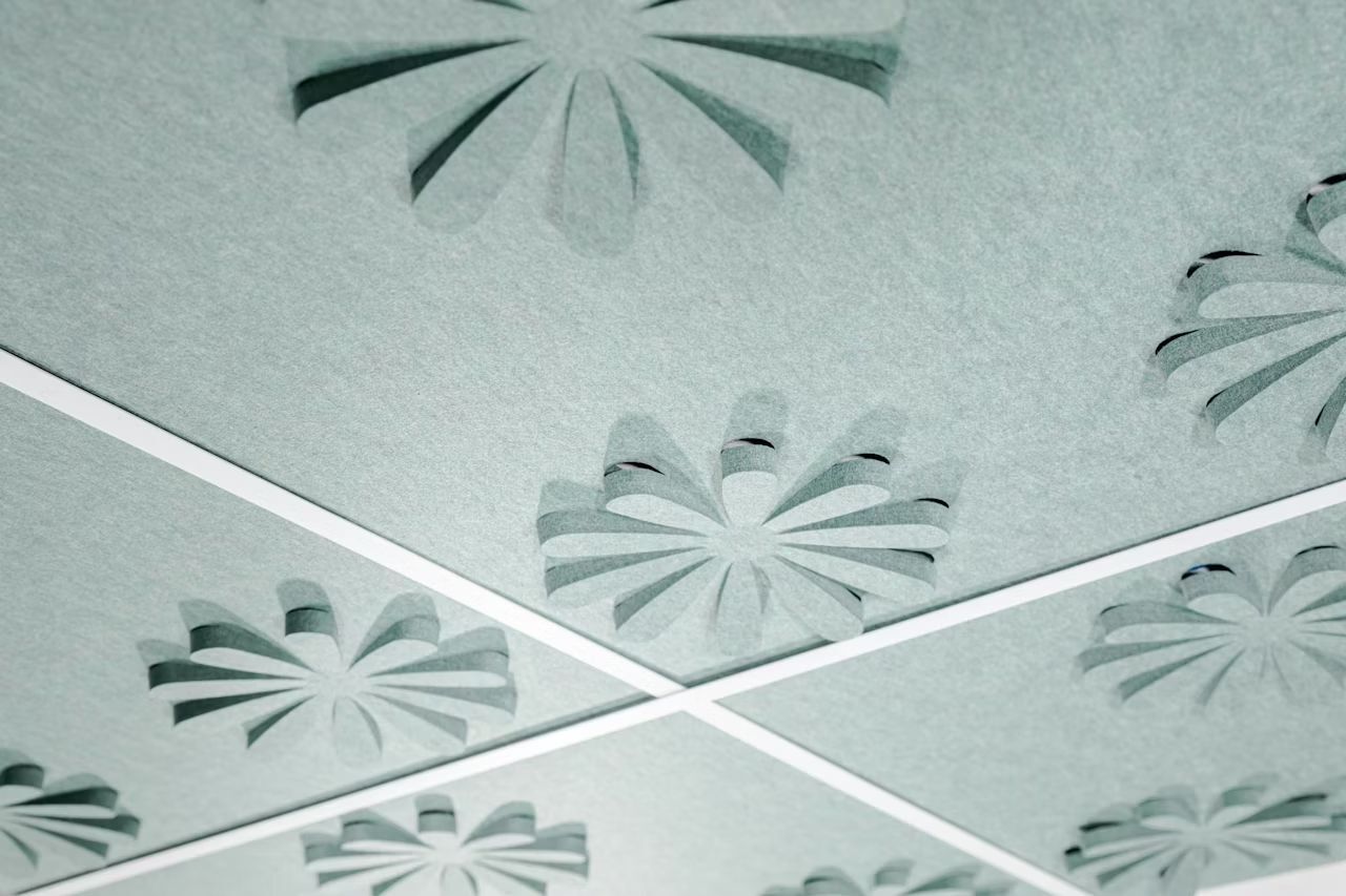 Graue Akustikplatten mit ausgestanzten Blumenmustern, an der Decke angebracht für Schallschutz und Ästhetik.