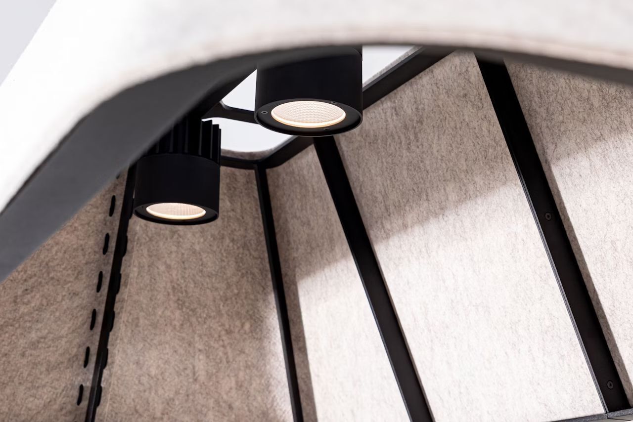 Nahaufnahme von zwei modernen schwarzen Deckenleuchten an einer strukturierten, hellgrauen Wandverkleidung.