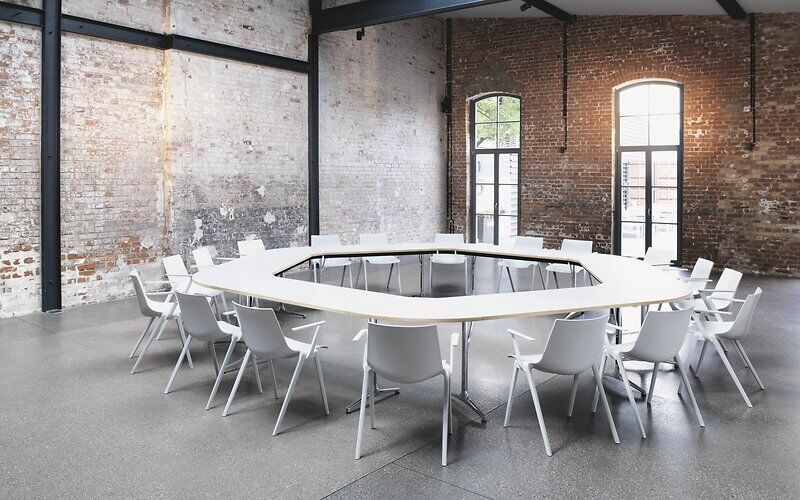 Moderner Besprechungsraum mit achteckigem Tisch und weißen ergonomischen Stühlen, umgeben von freiliegenden Ziegelwänden.