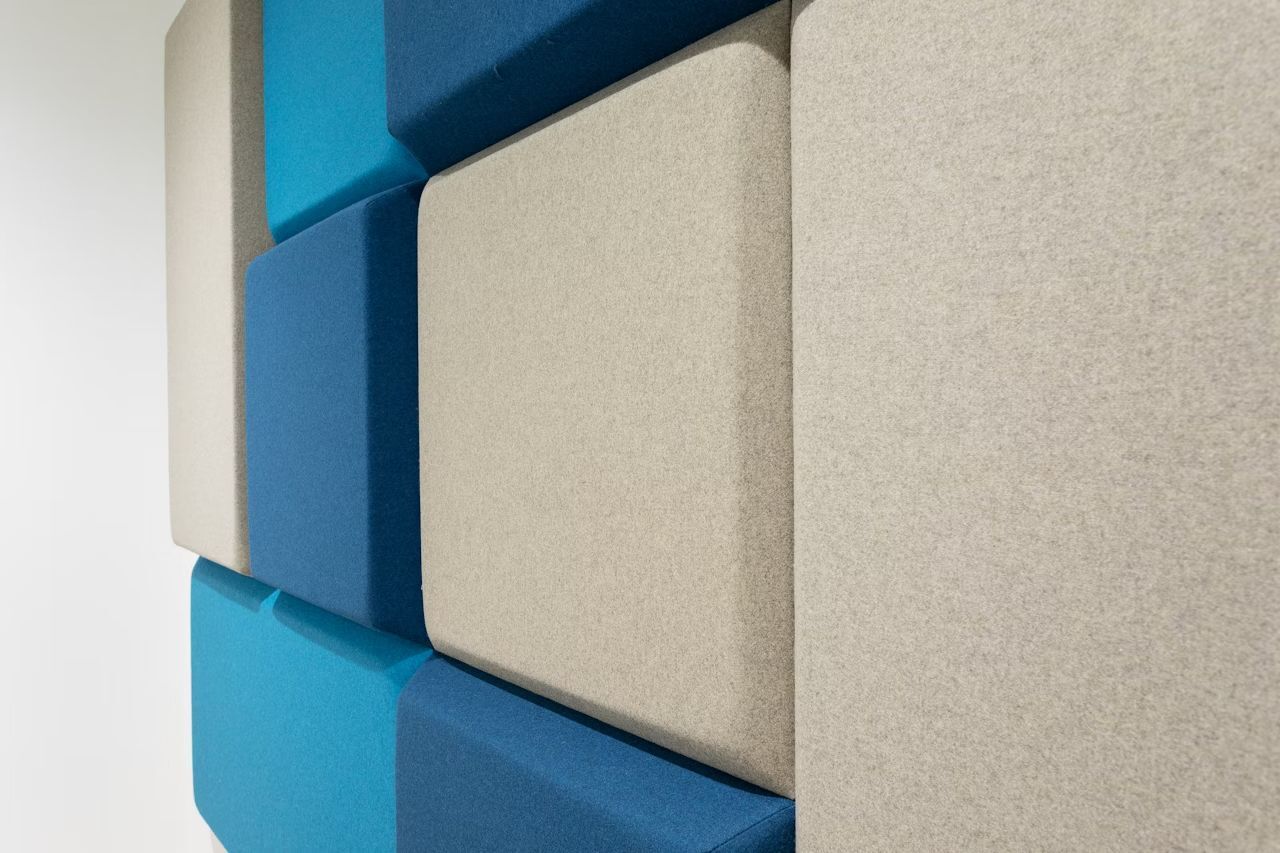 Wand aus schallabsorbierenden, farbigen Akustikpaneelen in Blautönen und Grau für Büroräume.