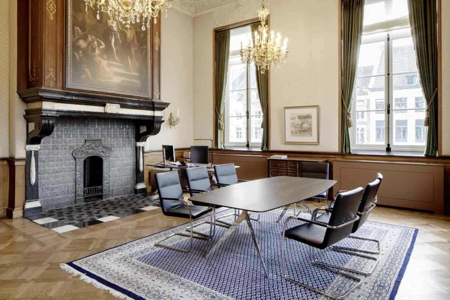 Elegantes Besprechungszimmer mit historischem Kamin, moderner Tischgruppe und luxuriösem Kronleuchter auf einem Teppich.