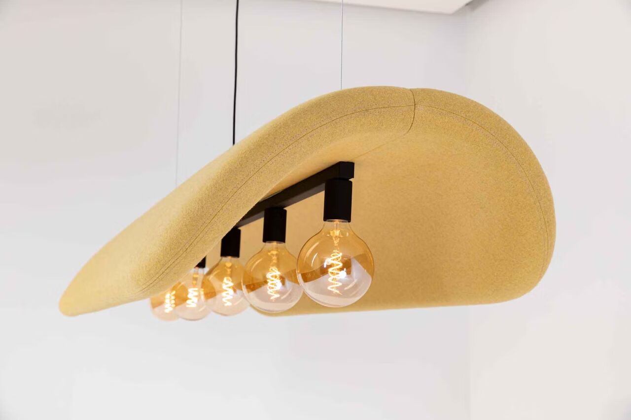 Designer-Pendelleuchte mit fünf Glühbirnen unter geschwungenem, gelbem Stoffschirm in modernem Interieur.