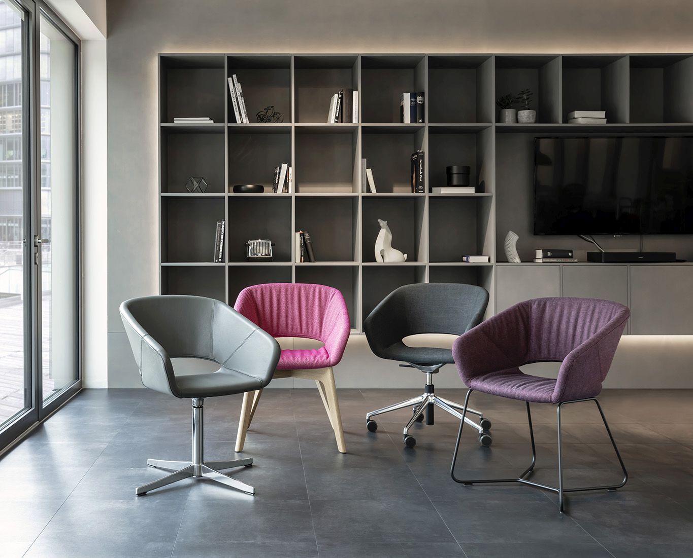 Vier stilvolle ergonomische Stühle in einem modernen Raum mit Regalwand im Hintergrund.