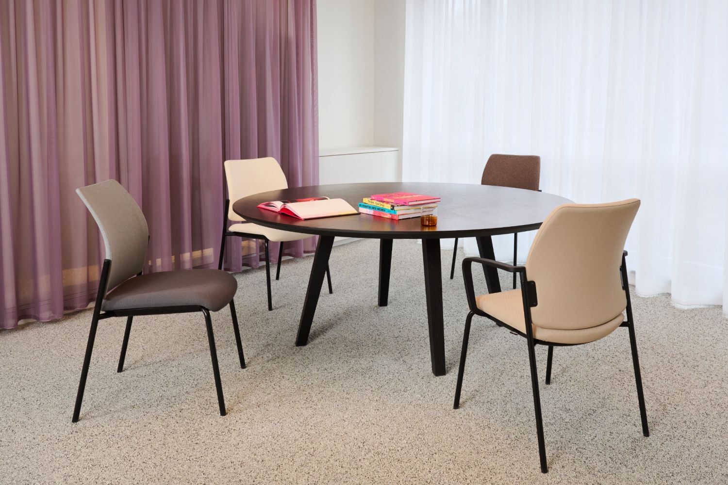 Runder Tisch mit vier ergonomischen Stühlen und Büchern in einem modernen Büro mit Vorhängen und Teppichboden.