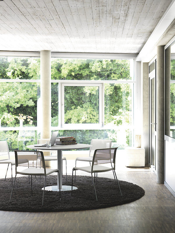 Moderne Büroumgebung mit ergonomischen Stühlen um einen Tisch vor großen Fenstern mit grüner Aussicht.