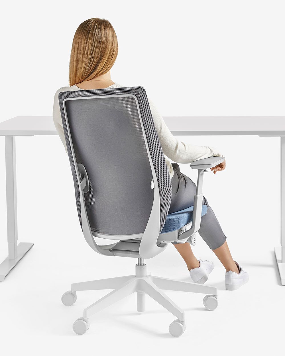 Frau sitzt in ergonomischem Bürostuhl vor einem Schreibtisch, betont rückenschonendes, dynamisches Sitzen.