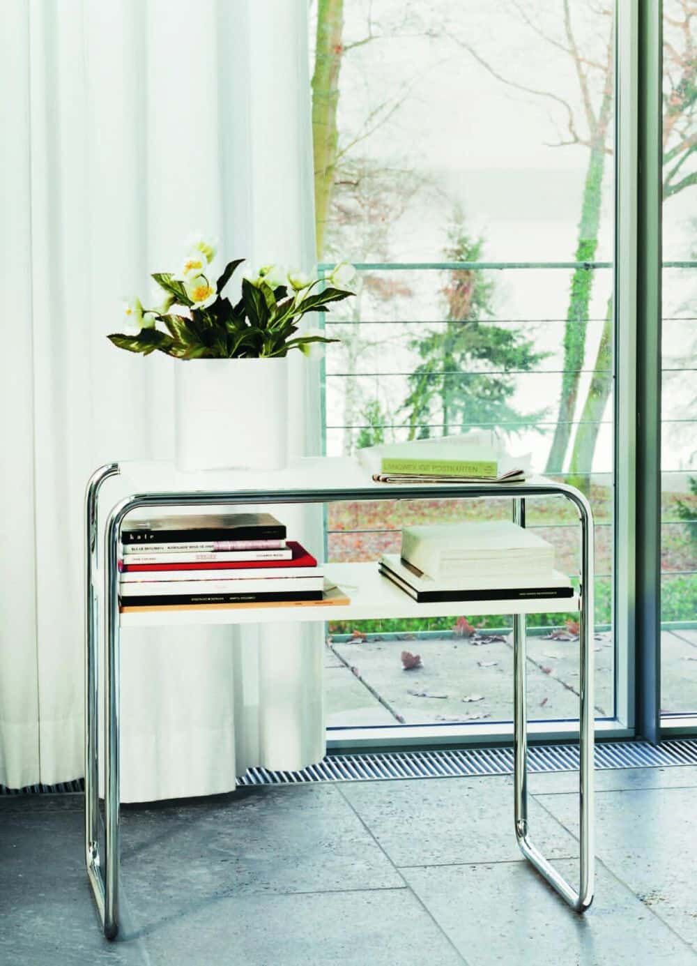 Moderner Beistelltisch mit Büchern und Blumentopf vor einem Fenster, lichtdurchfluteter Raum mit minimalistischer Einrichtung.
