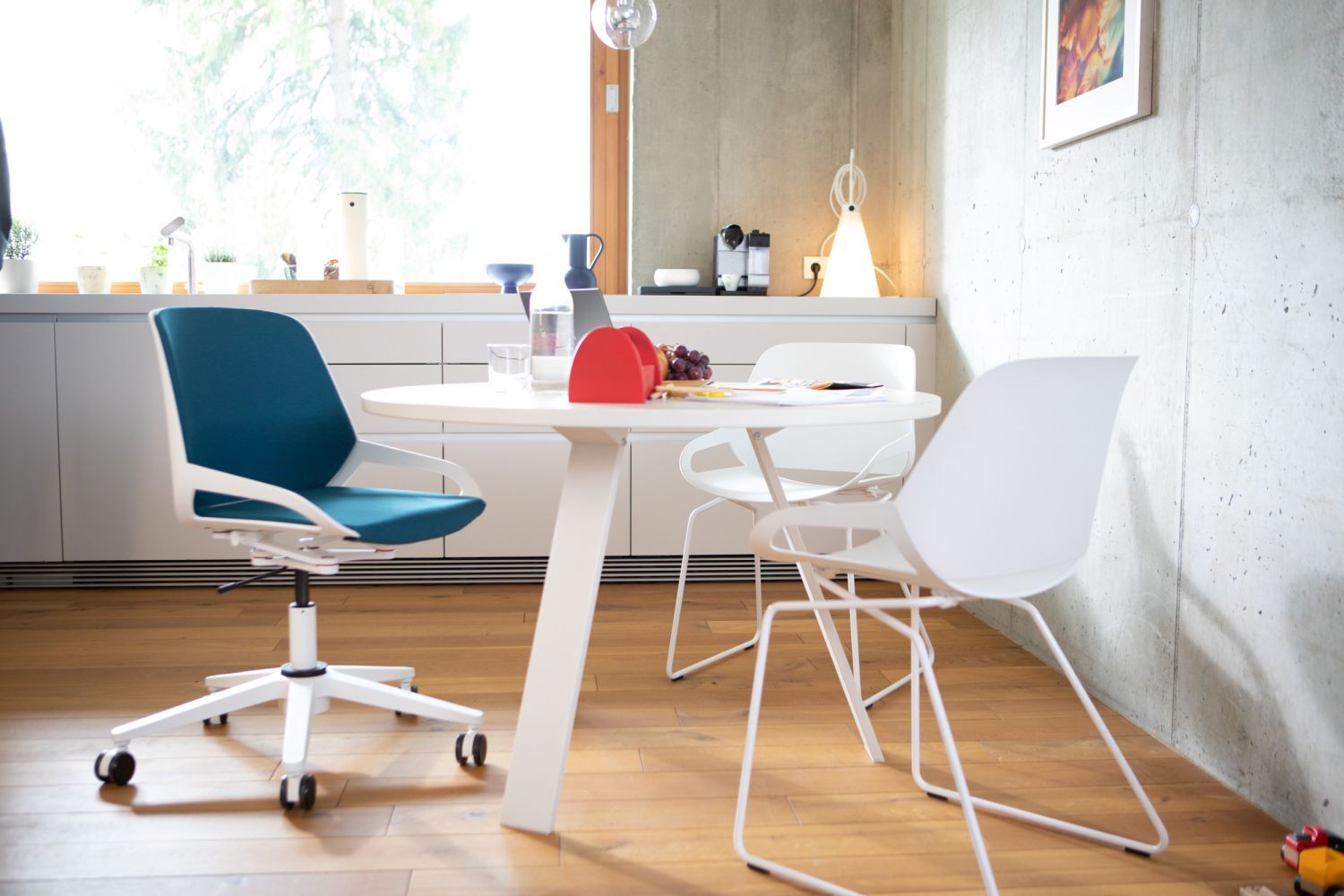 Moderner Essbereich mit ergonomischem Drehstuhl und weißen Stühlen an einem runden Tisch.