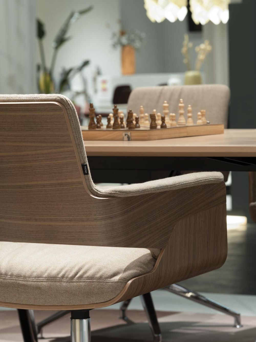 Schicker ergonomischer Stuhl in Holzoptik mit weicher Polsterung, im Hintergrund ein Schachspiel auf dem Tisch.
