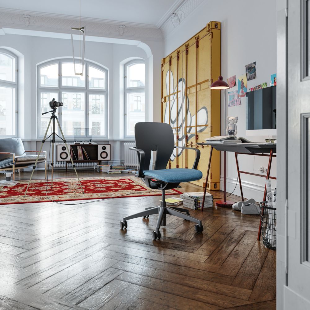 Ergonomischer Bürostuhl mit blauer Sitzfläche in einem modernen, lichtdurchfluteten Raum mit Parkettboden und dekorativem Teppich.