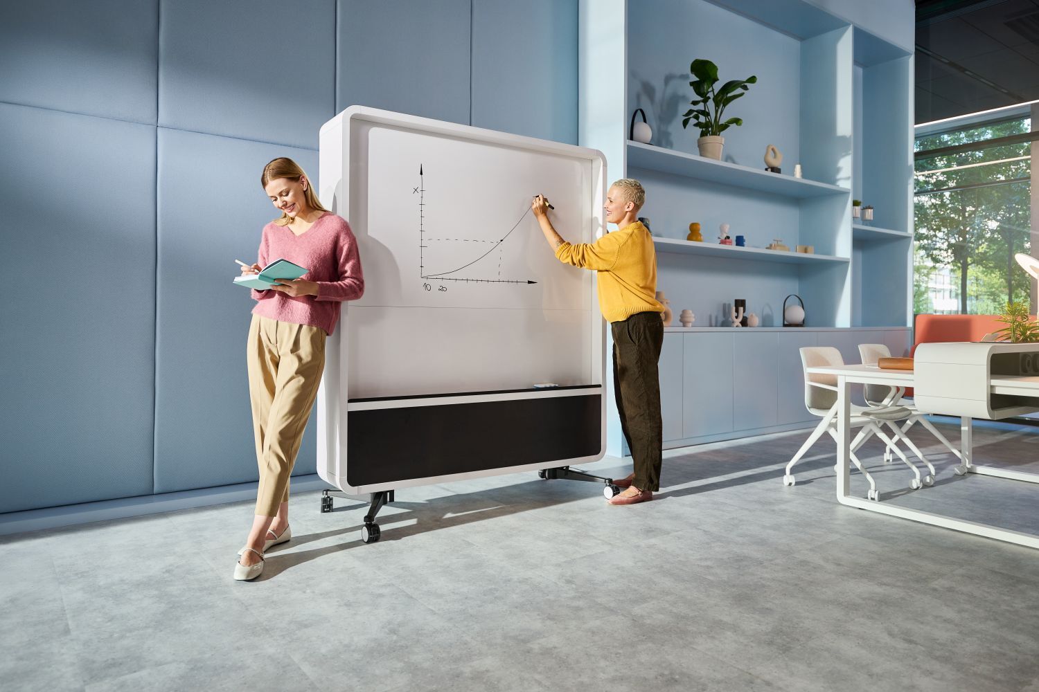 Zwei Personen arbeiten an einem Whiteboard in einem modernen Büro mit ergonomischen Möbeln.