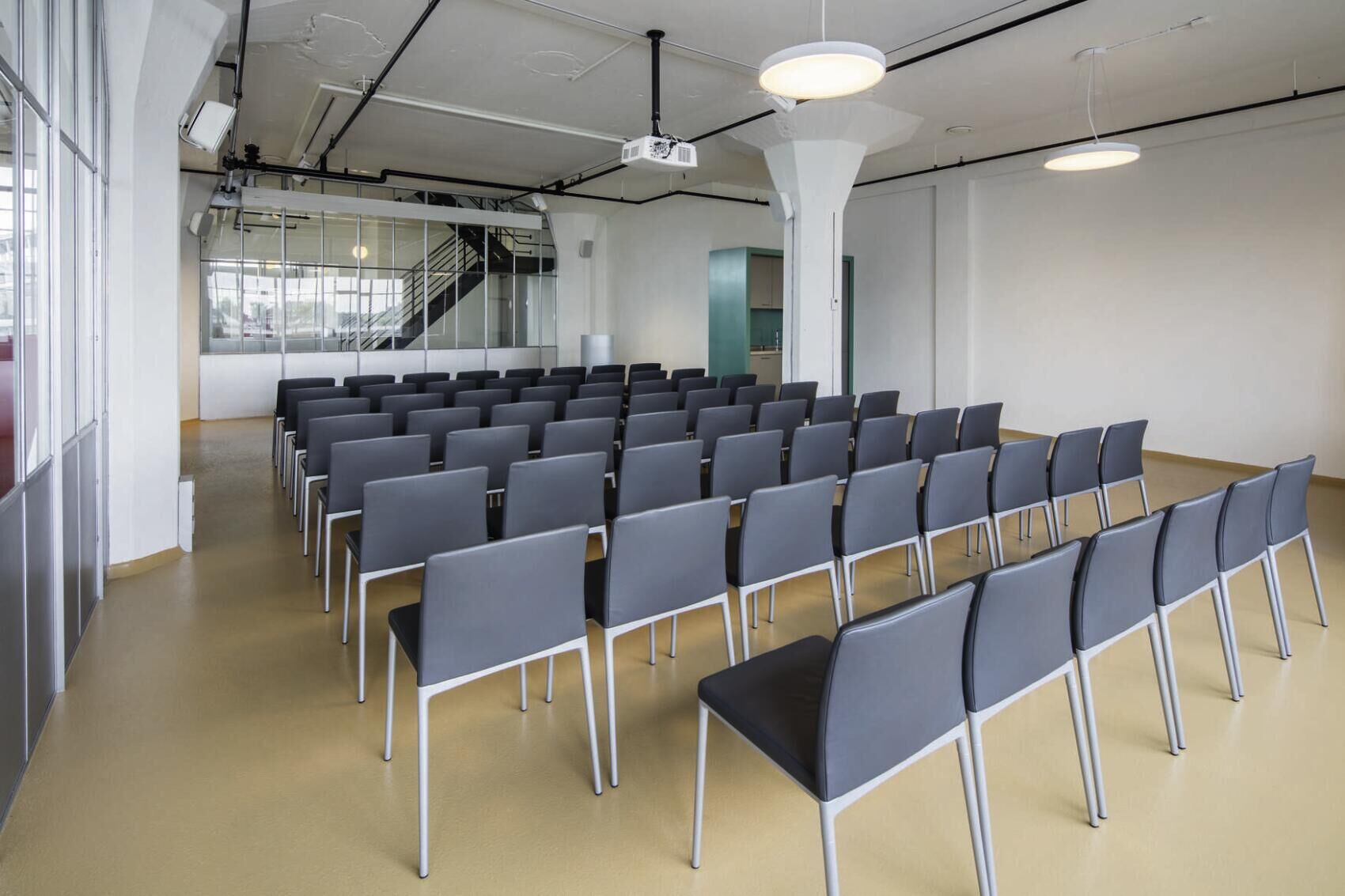 Modern eingerichteter Seminarraum mit grauen Stühlen und viel Tageslicht, geeignet für Konferenzen und Präsentationen.