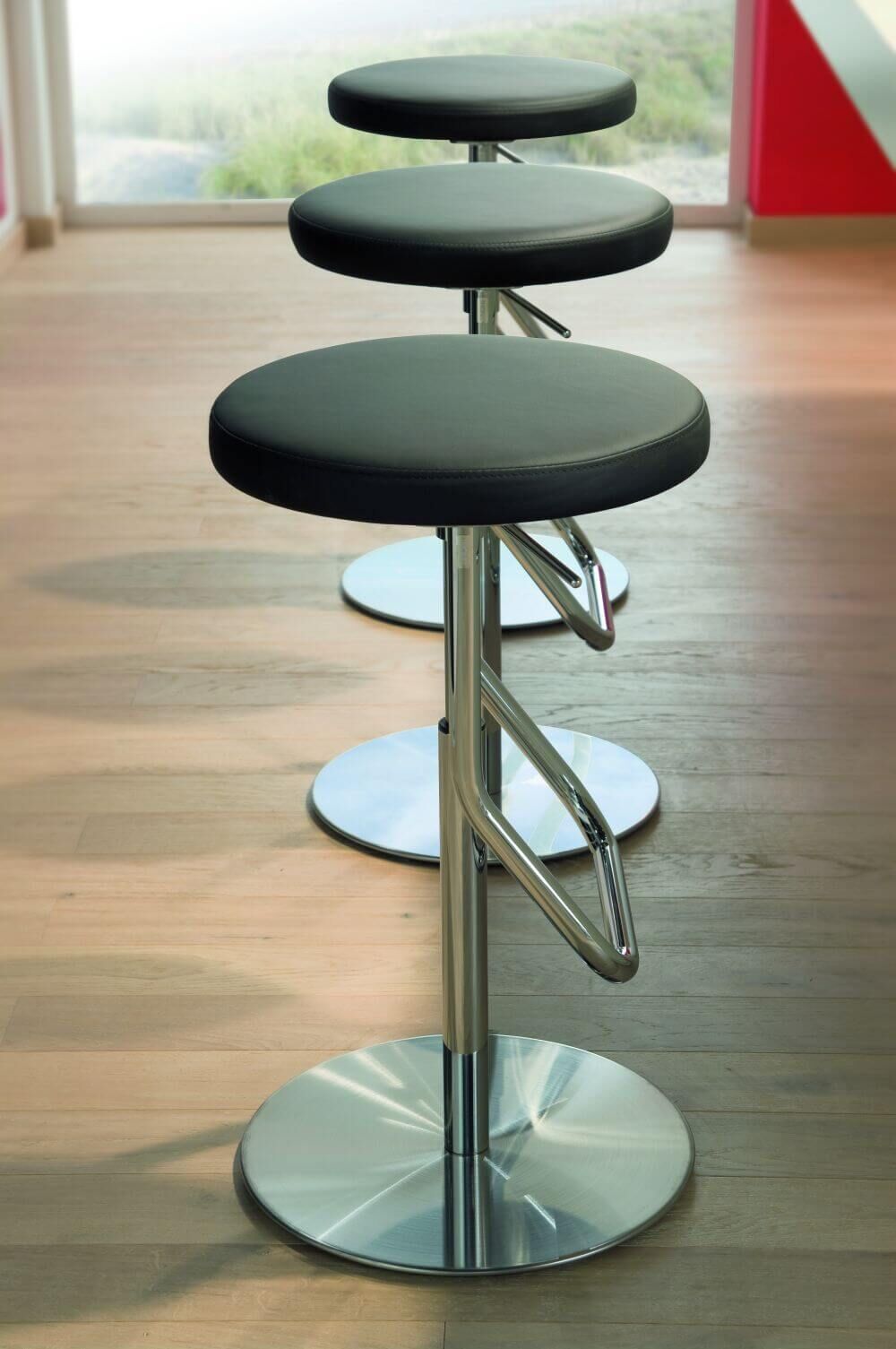 Drei elegante, ergonomische Hocker mit schwarzem Sitz und Chromfuß auf Holzboden in modernem Raum.