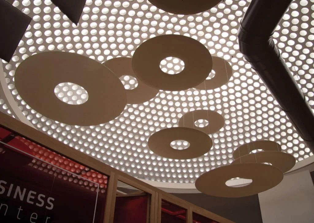 Moderne Innenraumdecke mit runden, hängenden Absorbern vor perforiertem Lichtdesign; stilvoll und akustisch optimiert.