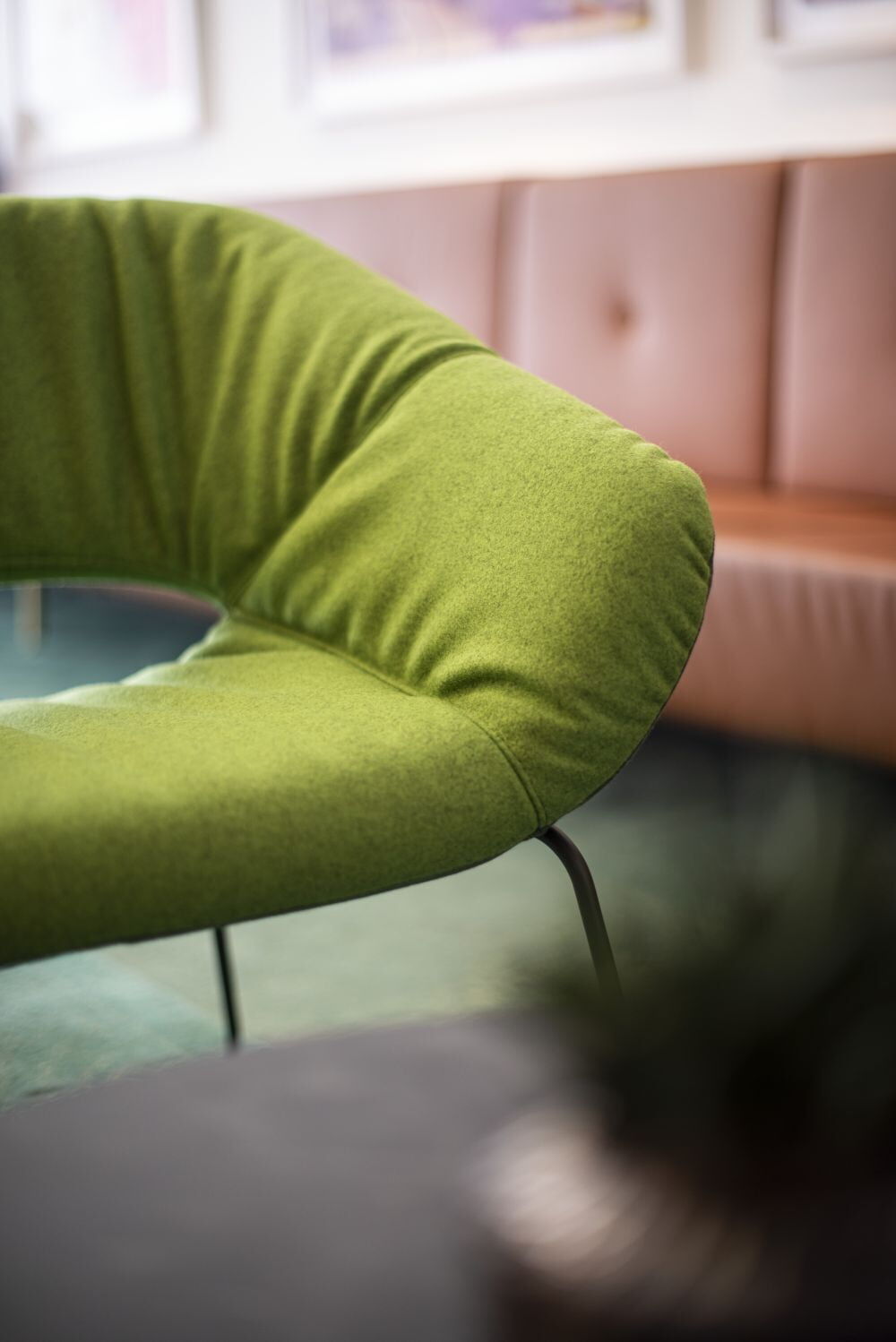 Detail eines modernen grünen ergonomischen Stuhls mit gebogener Lehne vor einem unscharfen Hintergrund.