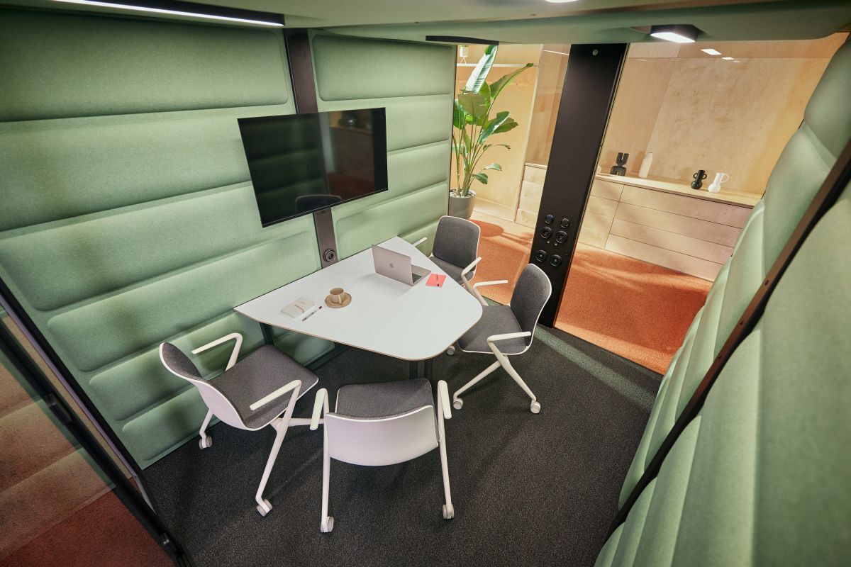 Moderne Besprechungsecke mit ergonomischen Stühlen, Tisch, Laptop und großem Bildschirm in grünem Raum.