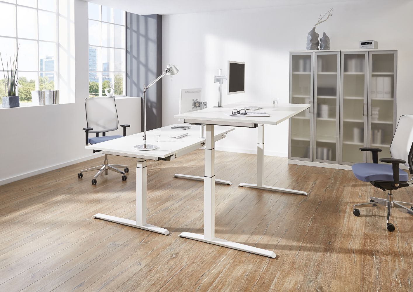 Moderner Büroraum mit ergonomischen Bürostühlen, einem höhenverstellbaren Schreibtisch und viel Tageslicht.