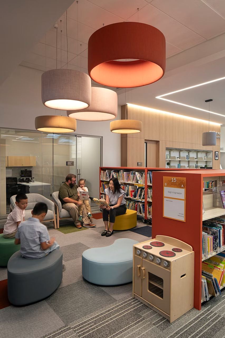 Kinderbereich in einer Bibliothek mit bunten Sitzkissen, Lesende Erwachsene und spielende Kinder.
