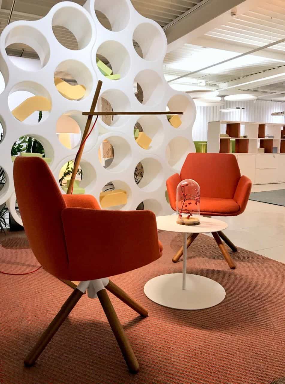 Zwei orangefarbene Sessel und ein runder Tisch in einem modernen Büro mit kreativem Raumteiler.