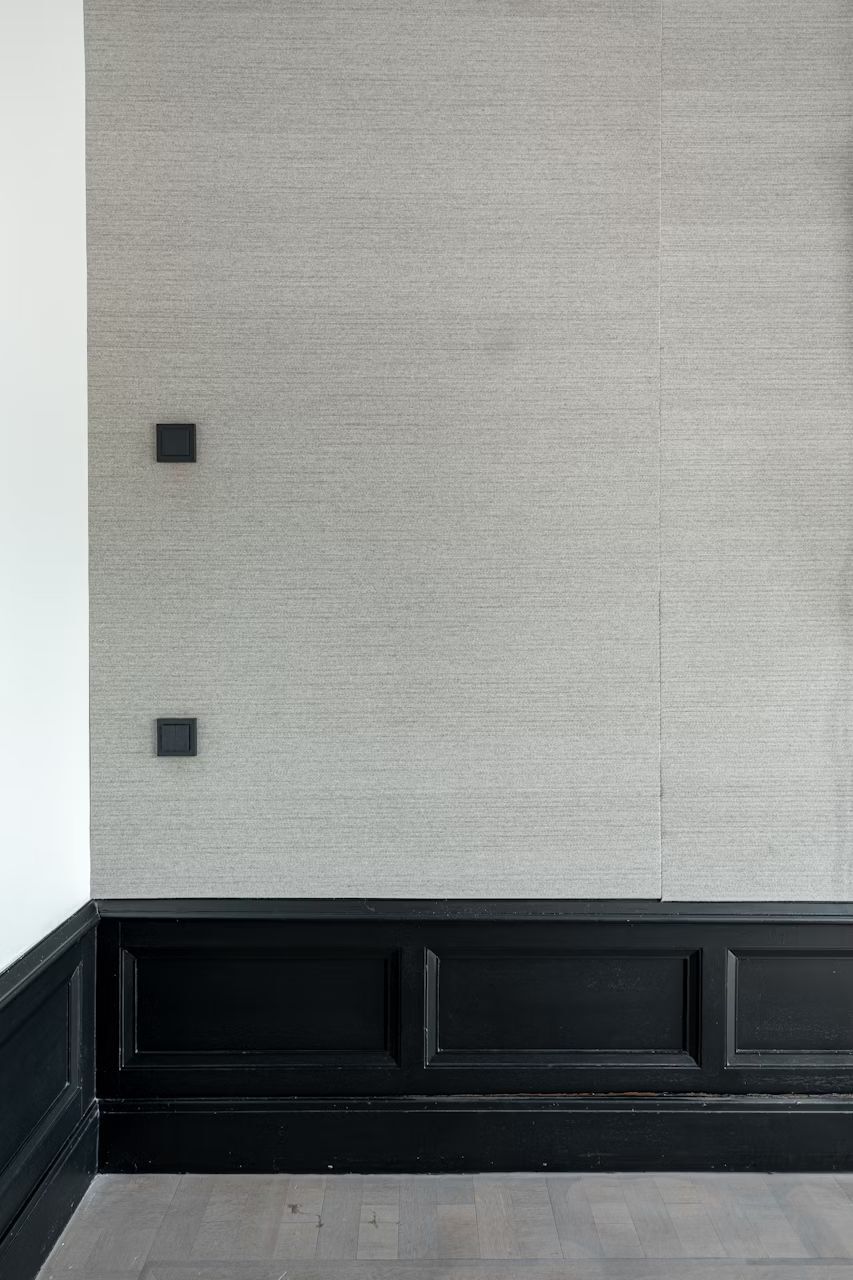 Hellgraue Wand mit schwarzen Leisten und zwei quadratischen Schalterplatten; minimalistisches Bürodesign.