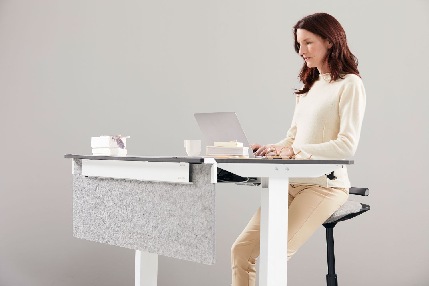 Frau sitzt ergonomisch an einem höhenverstellbaren Schreibtisch mit Laptop, förderlich für dynamisches Sitzen.
