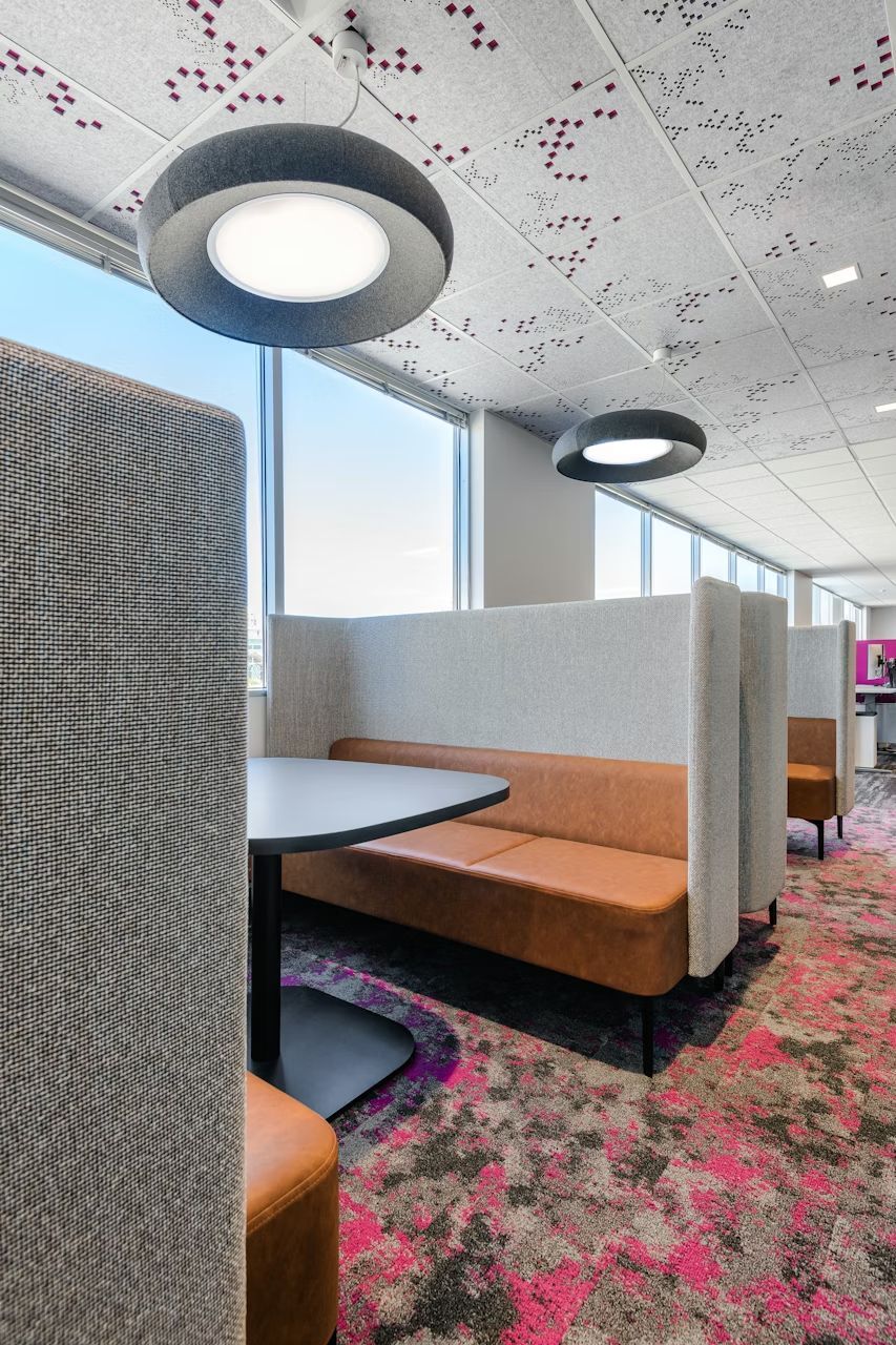 Moderne Büro-Lounge mit braunen Ledersofas, rundem Tisch und auffälliger Deckenbeleuchtung im ergonomischen Design.