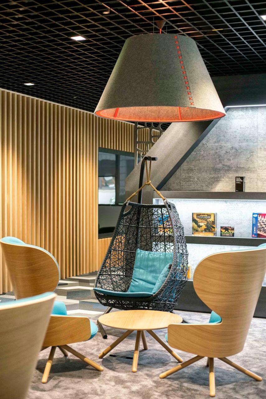 Moderne Lounge mit Hängesessel, Designer-Stühlen und Tisch, unter einer großen, stilvollen Lampe im Büroambiente.