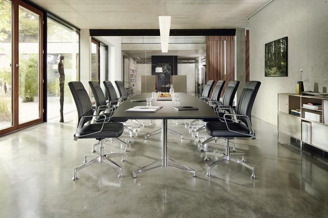 Moderner Besprechungsraum mit langen Tisch und ergonomischen Bürostühlen, umgeben von großen Fenstern und minimalistischer Dekoration.